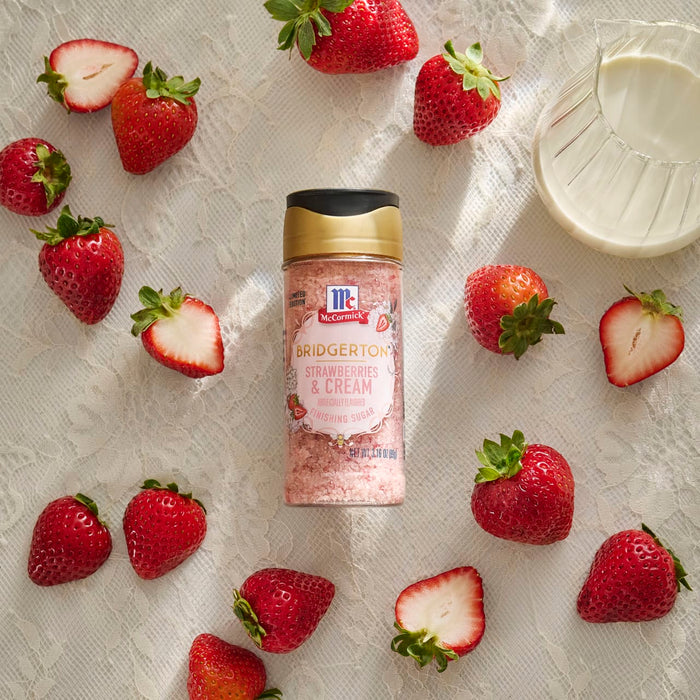 A bottle of McCormick Strawberry Extract is surrounded by fresh strawberries on a textured surface.