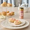 A two-tiered stand displays scones with McCormick Strawberry Flavored Sugar, alongside a teapot and a bowl of cream, suggesting a delightful tea time treat.