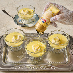 A hand wearing a glove is pouring Suntory liqueur over four servings of custard dessert topped with whipped cream and citrus zest.