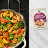 A skillet of stir-fried vegetables and chicken next to a McCormick Hibachi Chicken Rice seasoning packet.