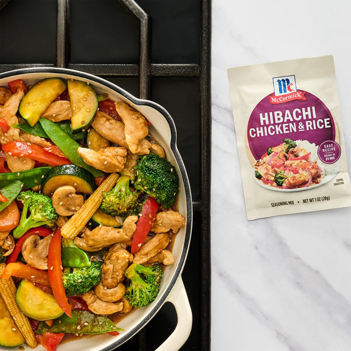 A skillet of stir-fried vegetables and chicken next to a McCormick Hibachi Chicken Rice seasoning packet.