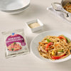 A plate of prepared V Mana Teriyaki Chicken Stir Fry is displayed next to an unopened package of the same product, along with a small bowl of sesame seeds.