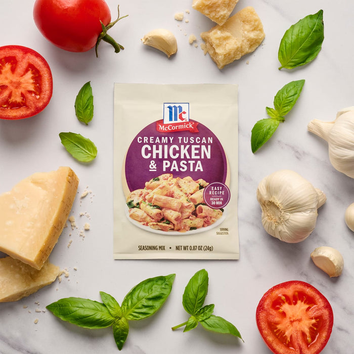 A packet of McCormick Creamy Tuscan Chicken &amp; Pasta mix is surrounded by fresh ingredients like tomatoes, garlic, basil, and parmesan cheese.