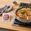 A package of McCormick Stir Fry Sauce Mix is displayed next to a pan of stir-fried noodles with beef and vegetables on a stovetop.