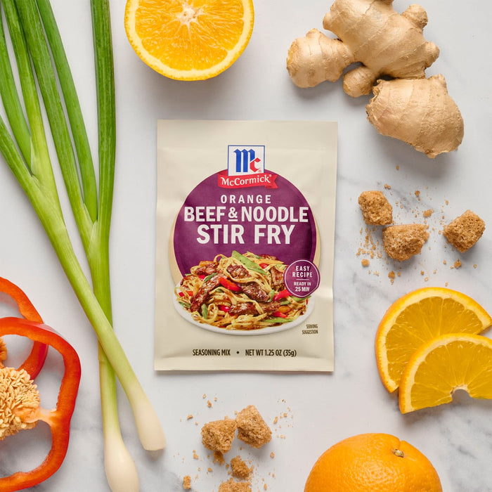 A packet of McCormick Beef &amp; Noodle Stir Fry seasoning mix is surrounded by fresh ingredients like ginger, oranges, and green onions.