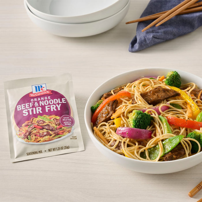 A bowl of beef and noodle stir fry with vegetables is displayed next to a McCormick Beef &amp; Broccoli Stir Fry seasoning packet.
