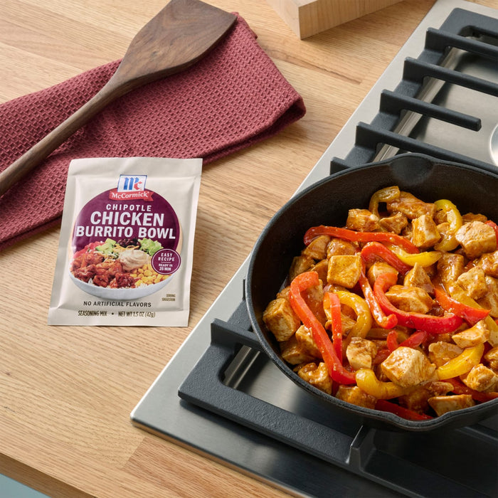 A packet of McCormick Chicken Fajita Skillet Sauce sits next to a cast iron skillet filled with cooked chicken and bell peppers on a stovetop.