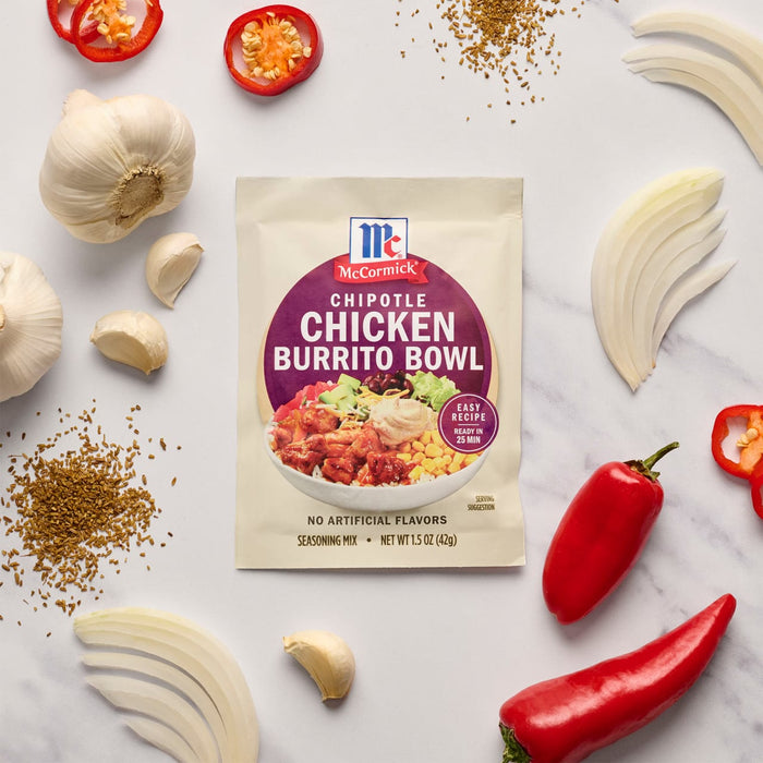 A packet of McCormick Chicken Burrito Bowl seasoning mix is surrounded by fresh ingredients like garlic, onions, and peppers.