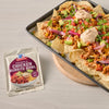 A sheet pan of nachos topped with chicken, avocado, and other toppings is displayed next to a packet of McCormick Chicken Burrito Bowl seasoning mix.