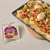 A sheet pan of loaded nachos with McCormick Chicken Burrito Bowl seasoning packet displayed next to it.