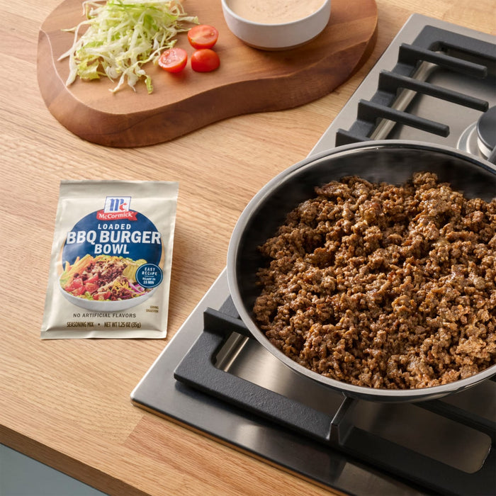 A packet of Maggi Fix fA?r Chili con Carne sits next to a pan of cooked ground beef, with shredded lettuce, tomatoes, and a bowl of sauce in the background, suggesting a meal preparation scene.