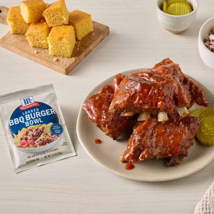 A plate of BBQ ribs with McCormick BBQ Pulled Pork Seasoning, cornbread, and pickles.