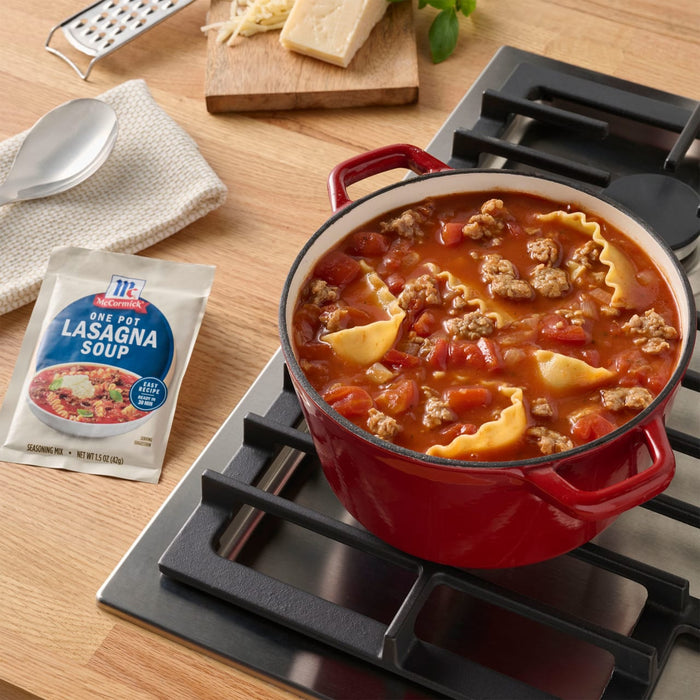 A pot of Progresso Lasagna Soup sits on a stovetop next to a packet of the same soup mix, with cheese and a grater in the background.