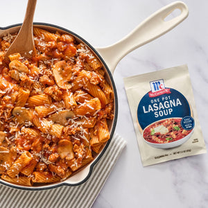 A skillet of lasagna soup with a wooden spoon and a packet of McCormick Lasagna Soup Mix.