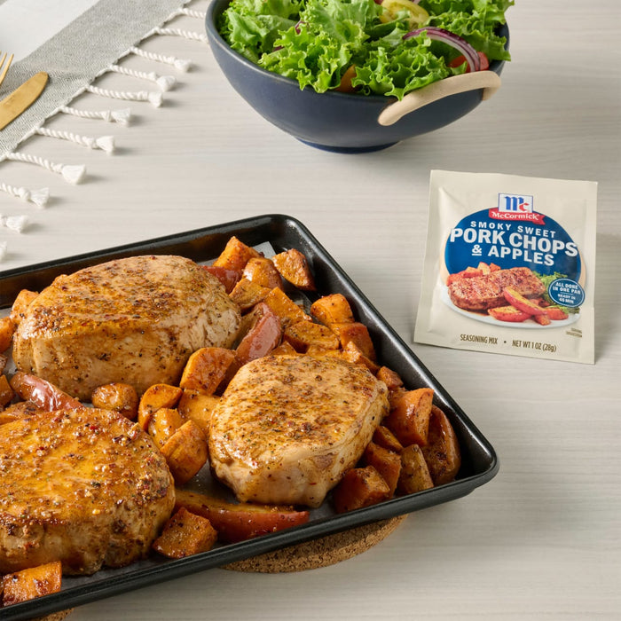 A sheet pan meal featuring McCormick Pork Chops and Apples seasoning mix, pork chops, and sweet potatoes, accompanied by a salad.