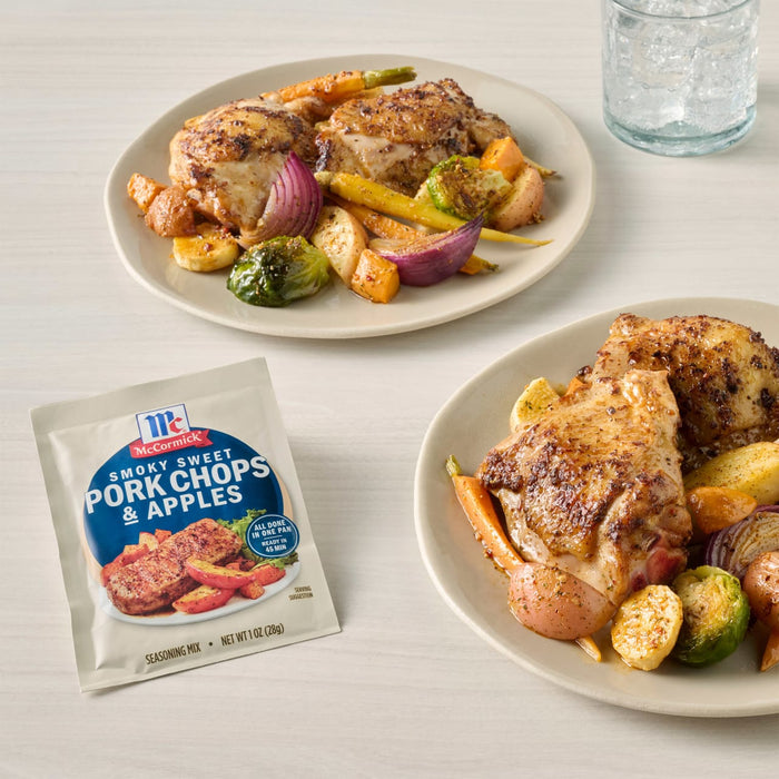 Two plates of pork chops and roasted vegetables are displayed next to a McCormick Slow Cookers Pork Chops &amp; Apples seasoning packet.