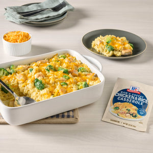 A prepared casserole dish of Uncle Ben's Chicken Broccoli Cheddar Rice is shown with a serving on a plate, a bowl of shredded cheese, and the product packaging.