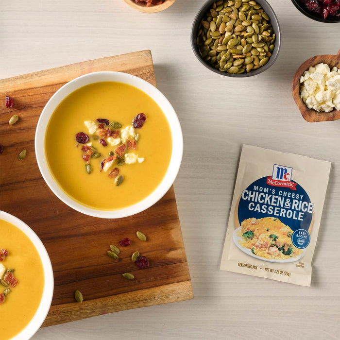 Two bowls of McCormick Butternut Squash Bisque are garnished with cranberries and pumpkin seeds, displayed on a wooden board next to a packet of the soup mix.