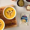 Two bowls of McCormick Butternut Squash Bisque are garnished with cranberries and pumpkin seeds, displayed on a wooden board next to a packet of the soup mix.