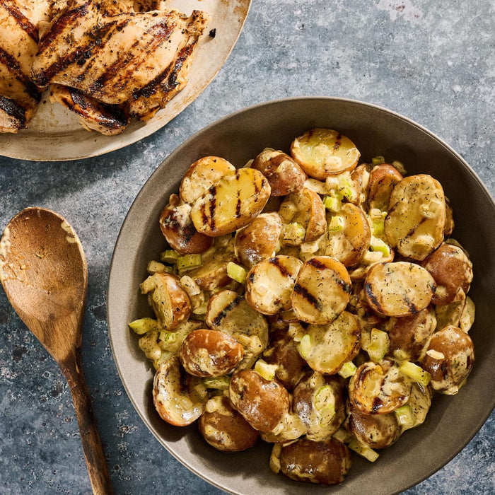 A bowl of grilled potato salad and a plate of grilled chicken are seasoned with Mccormick Grill Mates Buttermilk Dill Pickle Seasoning Mix 1.0 Oz on a blue textured surface.