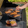 A person uses a basting brush to apply a glaze to salmon fillets on a grill next to a bowl of sauce and a package of Mccormick Grill Mates Tennessee Style Whiskey Honey Marinade Seasoning Mix 1.0 Oz.