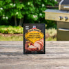 A package of Mccormick Grill Mates Tennessee Style Whiskey Honey Marinade Seasoning Mix, 1.0 Oz stands on a rustic wooden table with a grill and green foliage in the background.