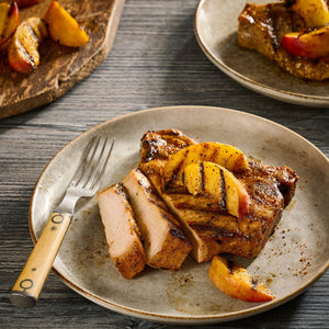 A grilled pork chop seasoned with Mccormick Grill Mates Tennessee Style Whiskey Honey Marinade Seasoning Mix, 1.0 Oz is sliced and served on a plate topped with charred peach wedges.