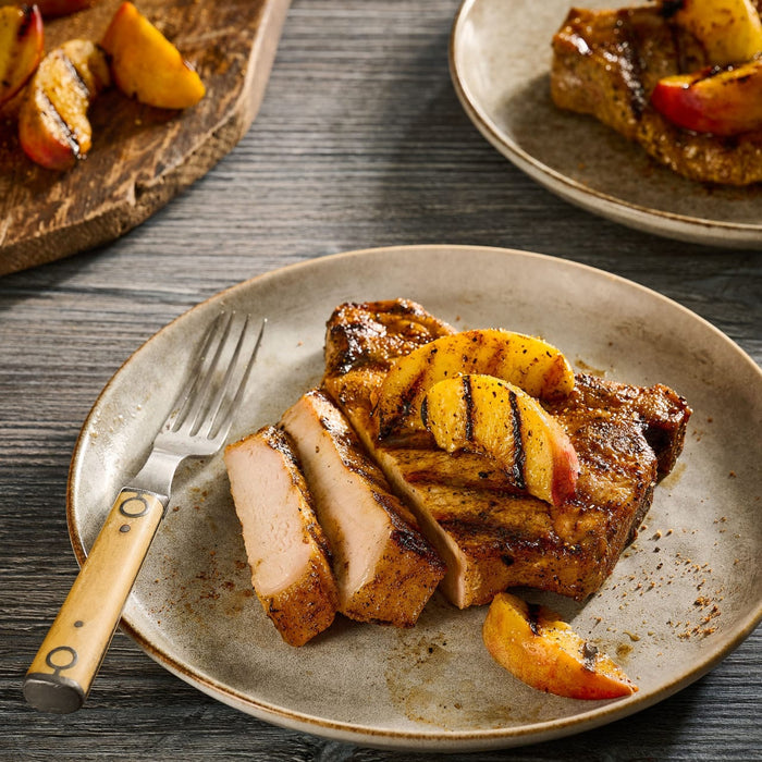 A grilled pork chop seasoned with Mccormick Grill Mates Tennessee Style Whiskey Honey Marinade Seasoning Mix, 1.0 Oz is sliced and served on a plate topped with charred peach wedges.