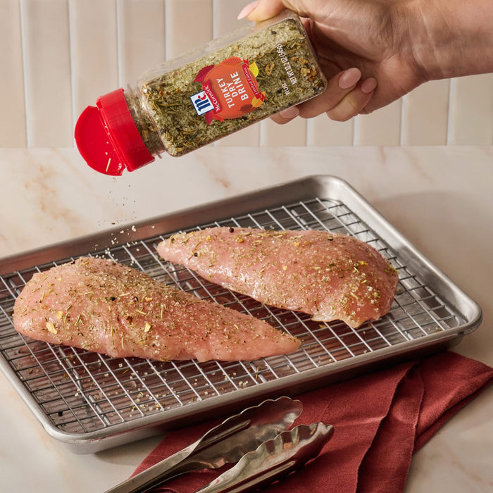 A hand seasons two raw turkey breasts on a wire rack with Mccormick Turkey Dry Brine Rub, 12.2 Oz to prepare them for roasting.