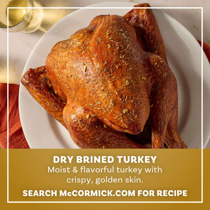 A whole roasted turkey with crispy golden skin seasoned with Mccormick Turkey Dry Brine Rub 12.2 Oz sits on a white platter next to a glass of white wine.
