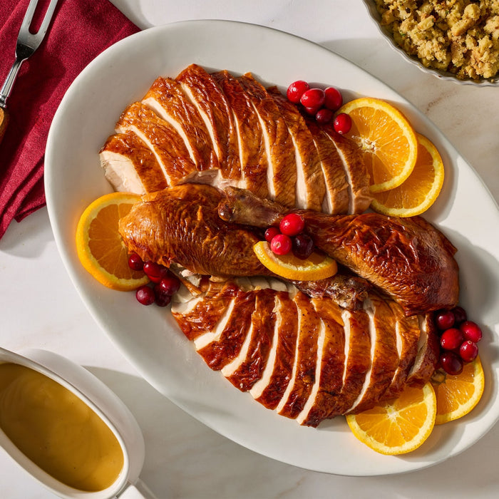 A white platter presents a beautifully roasted turkey prepared with Mccormick Turkey Dry Brine Rub, 12.2 Oz, sliced and garnished with fresh orange rounds and cranberries alongside gravy and stuffing.