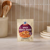 A packet of Mccormick Spicy Vodka Sauce Seasoning Mix, 1.0 Oz is displayed on a kitchen counter, with a utensil holder and plates in the background to suggest a home-cooked meal.