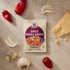 A packet of Mccormick Spicy Vodka Sauce Seasoning Mix, 1.0 Oz, is displayed on a marble countertop surrounded by fresh ingredients like red peppers, garlic, onion, and a wedge of Parmesan cheese.