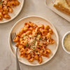 A top-down view of a plate of pasta in a creamy vodka sauce, made using Mccormick Spicy Vodka Sauce Seasoning Mix, 1.0 Oz, and garnished with grated cheese and fresh herbs.