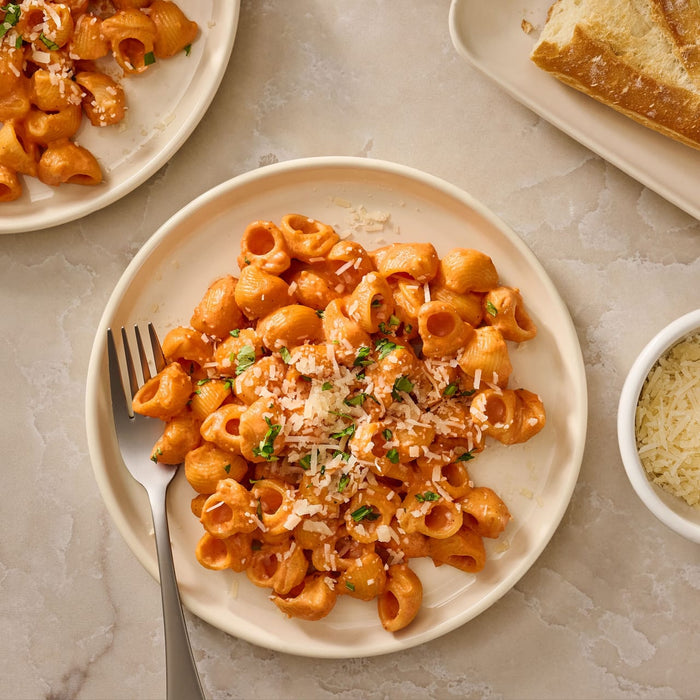 A top-down view of a plate of pasta in a creamy vodka sauce, made using Mccormick Spicy Vodka Sauce Seasoning Mix, 1.0 Oz, and garnished with grated cheese and fresh herbs.