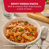 A close-up shot of a white bowl filled with spicy vodka pasta, made with the Mccormick Spicy Vodka Sauce Seasoning Mix, 1.0 Oz, and garnished with fresh basil and grated cheese, serves as an advertisement for the recipe.