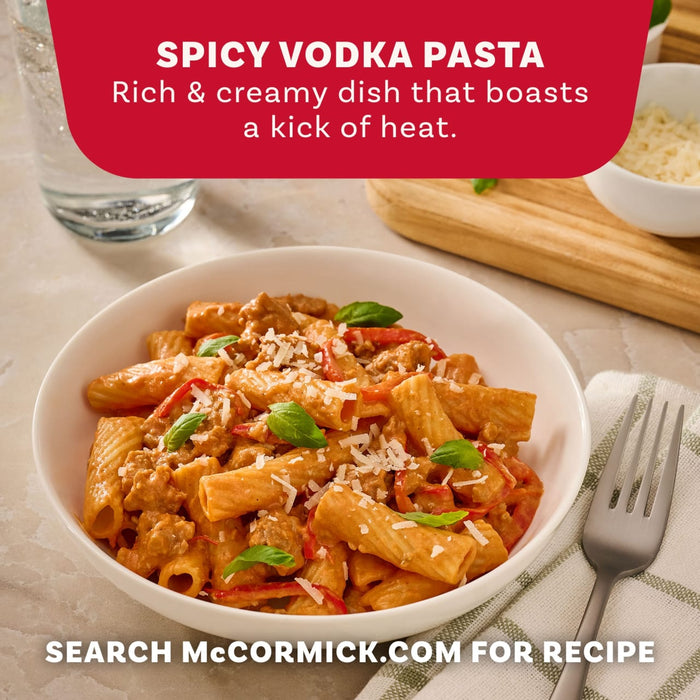 A close-up shot of a white bowl filled with spicy vodka pasta, made with the Mccormick Spicy Vodka Sauce Seasoning Mix, 1.0 Oz, and garnished with fresh basil and grated cheese, serves as an advertisement for the recipe.