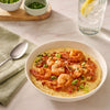 A delicious bowl of shrimp and grits, made using Mccormick Spicy Vodka Sauce Seasoning Mix, 1.0 Oz, is served in a white bowl next to a glass of water.