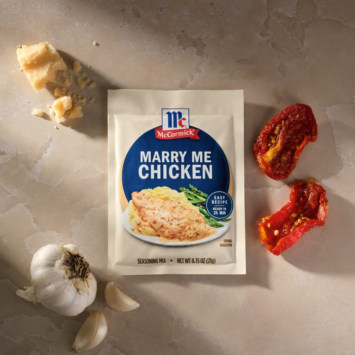 A packet of Mccormick Marry Me Chicken Seasoning Mix, 0.75 Oz, is displayed on a countertop surrounded by fresh ingredients like garlic, Parmesan cheese, and sun-dried tomatoes.