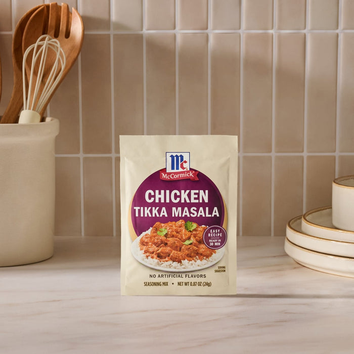 A packet of Mccormick Chicken Tikka Masala Seasoning Mix, 0.87 Oz, is displayed on a kitchen counter next to utensils and plates.