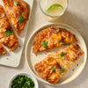 Slices of a delicious chicken tikka masala naan pizza, a creative meal made with Mccormick Chicken Tikka Masala Seasoning Mix, 0.87 Oz, are served on plates with a side of cilantro and a refreshing drink.