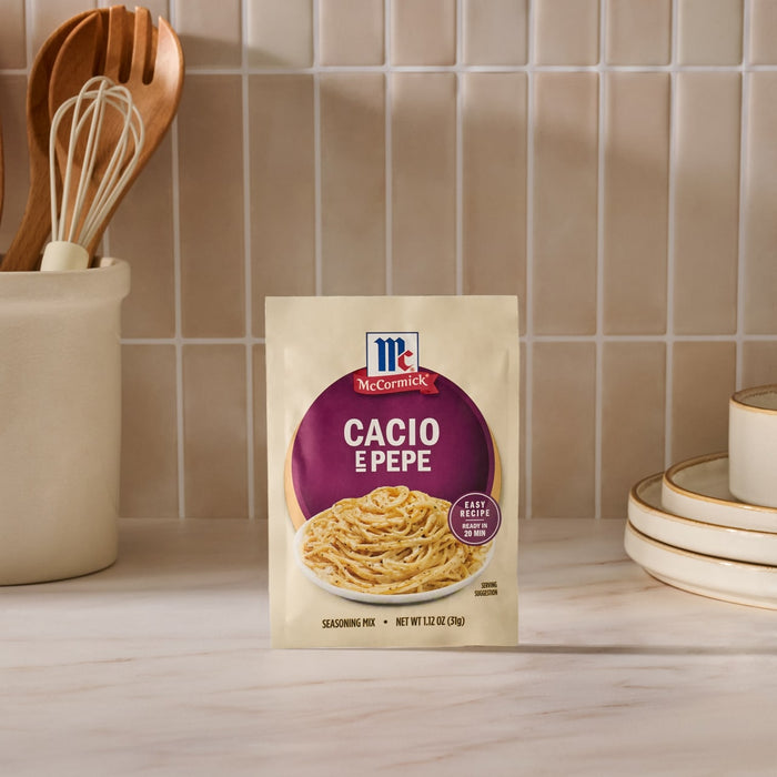 A packet of Mccormick Cacio E Pepe Seasoning Mix, 1.12 Oz, is displayed on a kitchen countertop in front of a tiled backsplash, with kitchen utensils and plates in the background.