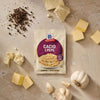 A packet of Mccormick Cacio E Pepe Seasoning Mix, 1.12 Oz is artfully arranged on a countertop with fresh ingredients like black peppercorns, chunks of cheese, pats of butter, and garlic.