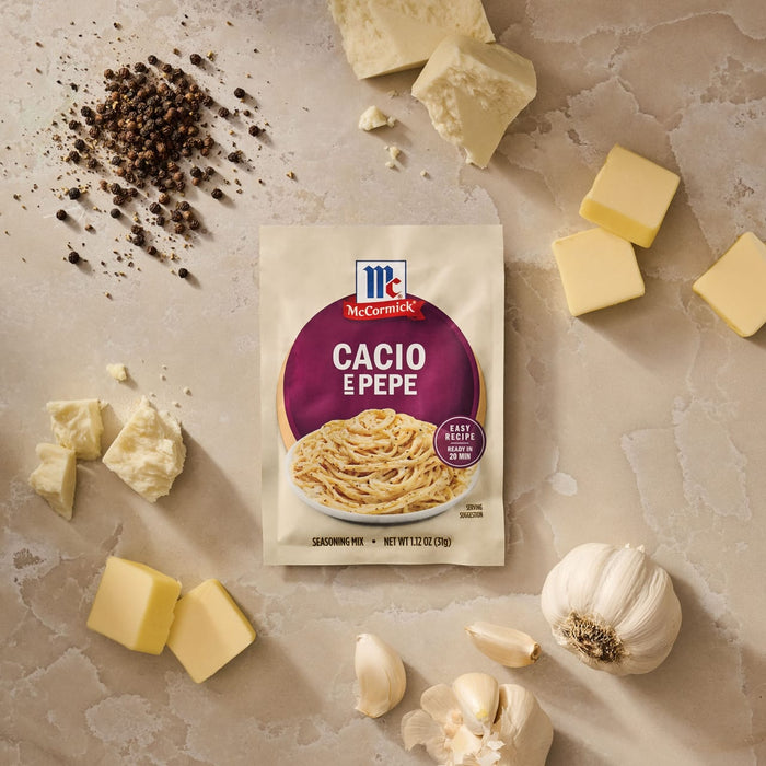 A packet of Mccormick Cacio E Pepe Seasoning Mix, 1.12 Oz is artfully arranged on a countertop with fresh ingredients like black peppercorns, chunks of cheese, pats of butter, and garlic.