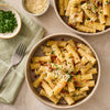 Two bowls of rigatoni pasta, prepared using Mccormick Cacio E Pepe Seasoning Mix, 1.12 Oz, are garnished with cheese, parsley, and bacon bits on a marble countertop.
