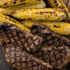 Grilled steaks with distinct grill marks are paired with grilled corn on the cob, suggesting a summer barbecue.