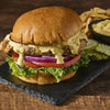 A delicious burger with lettuce, tomato, red onion, and a creamy sauce, served with fries and pickles.