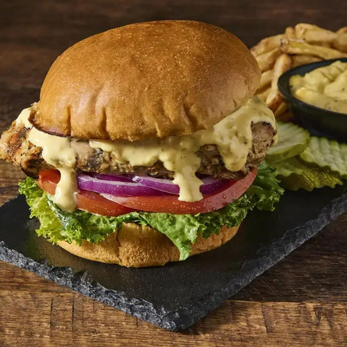 A delicious burger with lettuce, tomato, red onion, and a creamy sauce, served with fries and pickles.