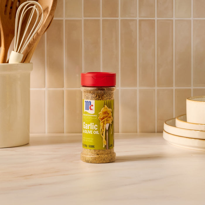 A bottle of Mccormick Garlic And Olive Oil Seasoning Blend, 5.25 Oz, sits on a kitchen counter next to utensils and plates.