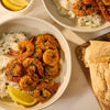 Two bowls of shrimp cooked with Mccormick Garlic And Olive Oil Seasoning Blend, 5.25 Oz, are served over white rice with a side of bread and lemon wedges.